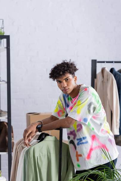 Empresário afro-americano olhando para a câmera perto de roupas no showroom  - Foto, Imagem