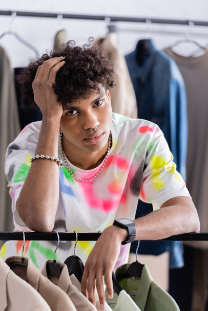 Африканский американский шоурум смотрит в камеру возле одежды на вешалке  - Фото, изображение