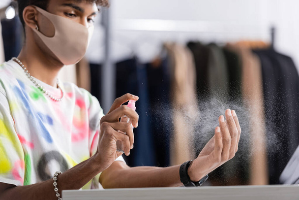Sanitizer nelle mani di un uomo d'affari afroamericano in maschera protettiva nello showroom  - Foto, immagini