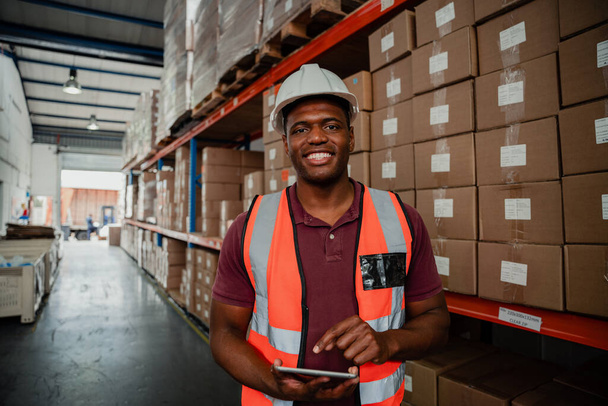 Smiling ethnic male businessman organising shipping information on digital tablet standing in warehouse. - Foto, Bild