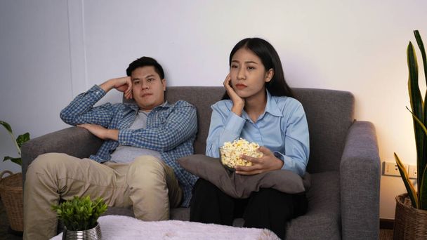 Щаслива молода азіатська пара кладе диван у своїй затишній вітальні, дивиться фільм на телебаченні та їсть попкорн разом увечері вдома
 - Фото, зображення