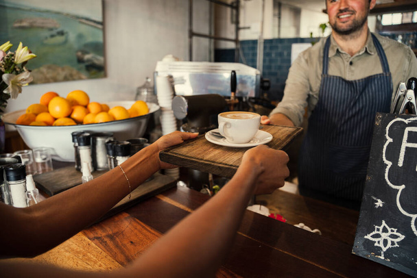 Smiling waiter handing fresh hot latte to woman in funky cafe  - Foto, Imagem