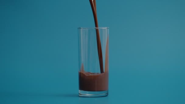 Super lento movimento di versare latte al cioccolato in vetro trasparente, sfondo blu  - Filmati, video