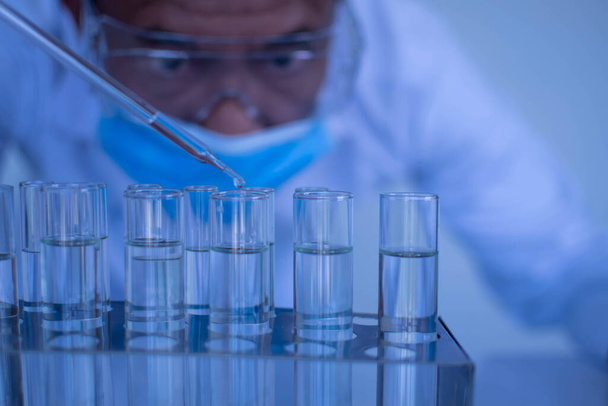 Άνδρας επιστήμονας φορώντας προστατευτικά γυαλιά στάζει χημικά τεστ ένα εμβόλιο. Βιοχημικοί διεξάγουν πειράματα για να ανακαλύψουν νέα φάρμακα. Ερευνητές εργάζονται σε επιστημονικά εργαστήρια. Κλείσιμο, αυτοσυγκέντρωση - Φωτογραφία, εικόνα