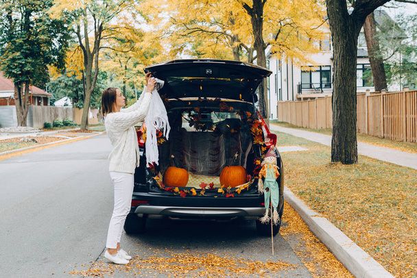 Karkki tai takakontti. Halloween autossa. Nainen koristelu ajoneuvon perinteisen lokakuun loma ulkona. Punaiset kurpitsat, variksenpelätin, syksyn syksyn lehdet juhlan kunniaksi kuorma-auton takana.  - Valokuva, kuva