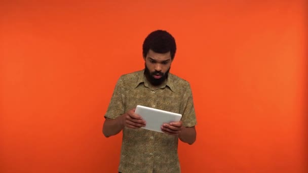 Африканский американец играет в видеоигру на цифровом планшете, изолированном на оранжевом - Кадры, видео