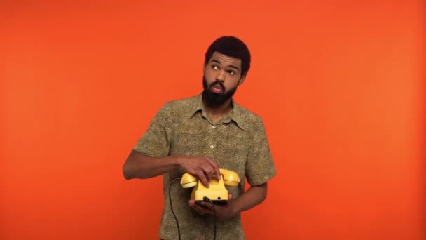 Αφροαμερικάνος μιλάει στο κίτρινο ρετρό τηλέφωνο απομονωμένος στο πορτοκαλί. - Πλάνα, βίντεο