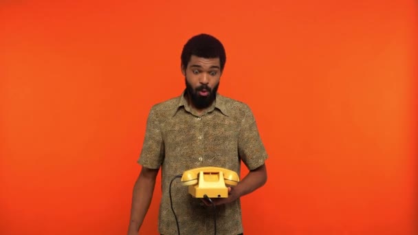 uomo afroamericano scontento di parlare al telefono retrò isolato su arancione - Filmati, video