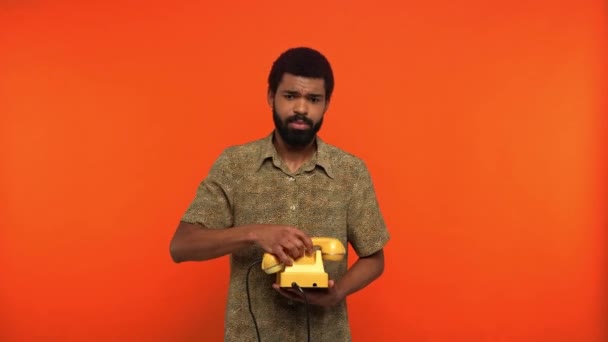 オレンジに隔離されたレトロな電話で話すアフリカ系アメリカ人 - 映像、動画