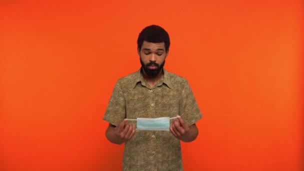 uomo afroamericano indossando maschera medica isolato su arancione - Filmati, video