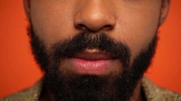 μερική άποψη του γενειοφόρου της Αφρικής Αμερικανός άνθρωπος γλείφει τα χείλη απομονώνονται σε πορτοκαλί - Πλάνα, βίντεο