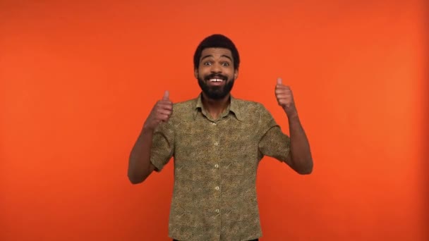 hombre afroamericano positivo mostrando pulgares hacia arriba aislado en naranja - Imágenes, Vídeo