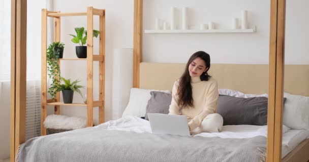 Ajattelevainen nainen käyttää kannettavaa tietokonetta sängyssä - Materiaali, video