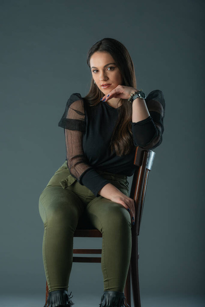 attractive brunette model sitting on a old chair posing and looking at camera on grey background - Photo, Image