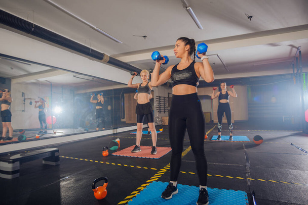 Gruppe athletischer junger Frauen in Sportbekleidung mit Kurzhanteln beim Training im Fitnessstudio - Foto, Bild