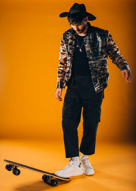 Studio tělo záběr trendy mladý muž na sobě moderní styl oblečení na skateboardu - Fotografie, Obrázek