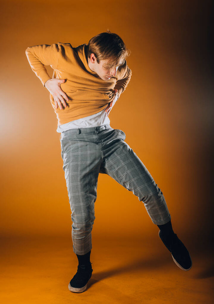 Bailarina masculina caucásica ejercitando un baile contemporáneo en la pared naranja - Foto, Imagen
