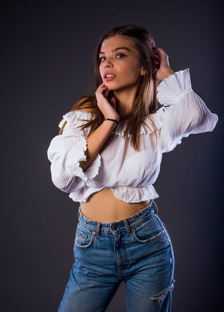 Portrait of a female model posing in trendy denim jeans against dark background - Photo, image