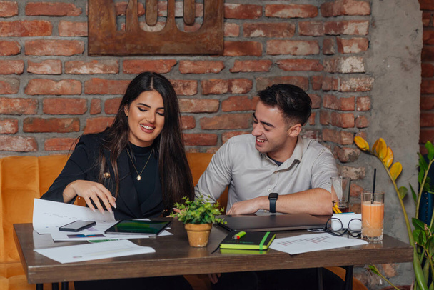 Επιτυχημένοι νέοι επιχειρηματίες που μοιράζονται ιδέες και χαμογελούν ενώ εργάζονται μαζί σε ένα έργο σε μια καφετέρια. - Φωτογραφία, εικόνα