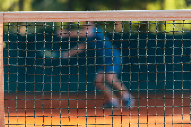 Strong male tennis player observed through the tennis net - Fotoğraf, Görsel