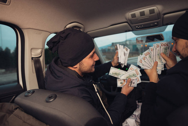 Zwei glückliche Bankräuber feiern ihren erfolgreichen Schlag, während sie in dem Auto sitzen, das sie für den Überfall benutzt haben. - Foto, Bild