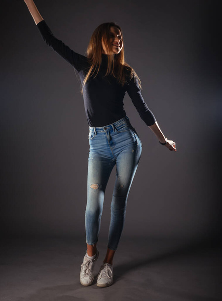 Attractive female model in denim jeans posing isolated on grey background. - Фото, изображение