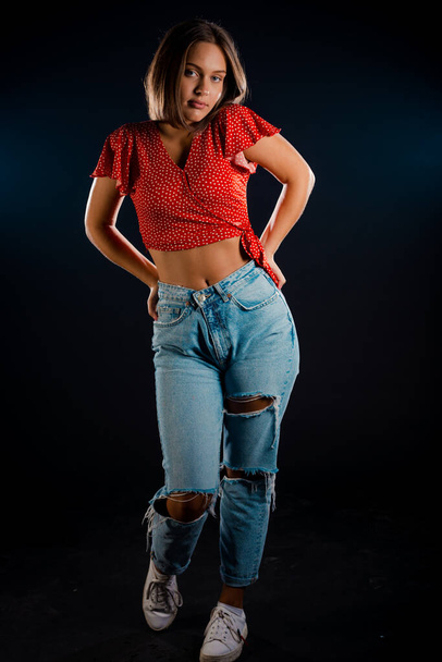 Portrait de mode studio d'une fille moderne portant un pantalon en denim élégant et un haut rouge - Photo, image