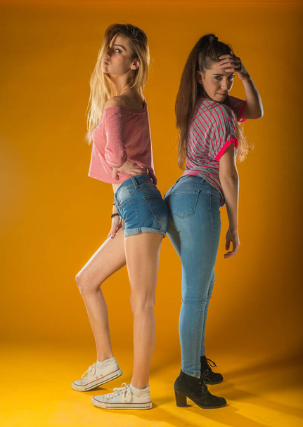 Romantische Freundinnen in trendigen Klamotten stehen auf gelbem Hintergrund. Unbekümmerte Mädchen senden Luftküsse. - Foto, Bild