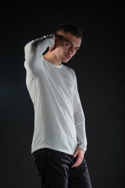 Fashion portrait on a black background of a handsome male model in white blouse and black pants - Foto, Imagen