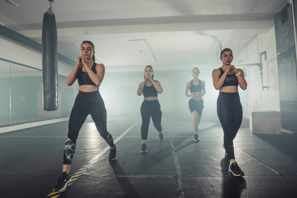 Grupa sportowców w odzieży sportowej robi ćwiczenia longe na siłowni prawą nogą - Zdjęcie, obraz