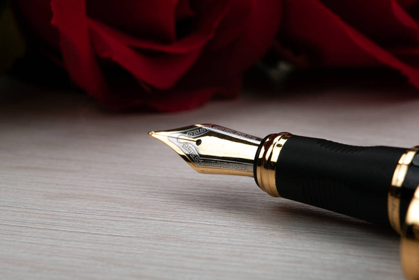 pluma dorada con rosas rojas en un primer plano de mesa de madera - Foto, imagen