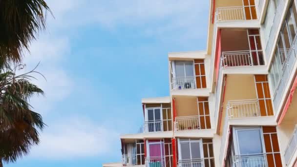 Laag uitzicht op oud appartement gebouw balkons en ramen met luifel zachtjes bewogen door de wind tegen de blauwe lucht op zonnige dag in Spanje - Video