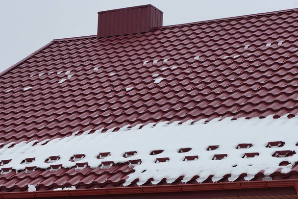 one metal chimney on a red tiled roof of a private house in white snow on a winter street against a gray sky - Fotoğraf, Görsel