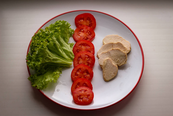 Sabroso desayuno dietético en un plato de hojas de ensalada, tomates en rodajas y brisket de pollo hervido - Foto, Imagen