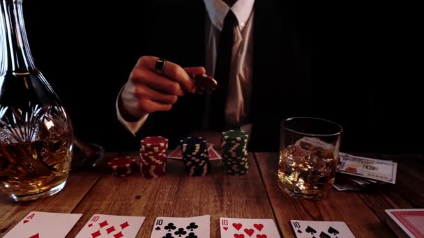 Богатый человек в черном костюме бросает фишки в покер, сидя за столом, где есть карты - Кадры, видео