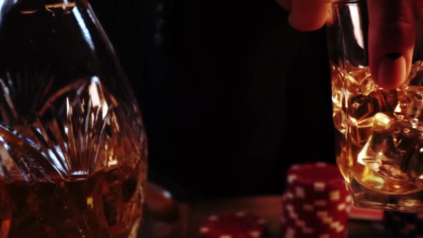 Macro beelden van de mens hand met manicure die glas vol whisky met ijs vasthoudt en mengt - Video
