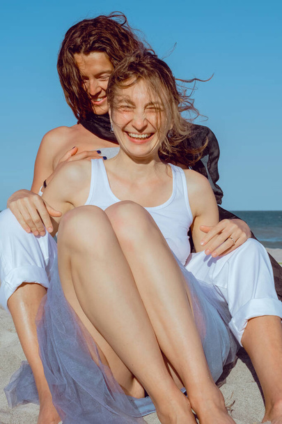 Gelukkig homostel brengt gelukkige tijd samen door. Een paar lesbiennes hebben plezier op het strand. Mooie vriendinnen ontspannen zich buiten. Lifestyle lesbisch paar concept. - Foto, afbeelding