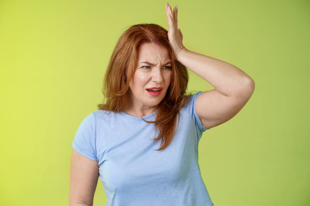 Something important slip my mind. Concerned worried upset redhead mature woman punch forehead turn away frustrated frowning disappointed forget cancel appointment stand green background - Photo, Image