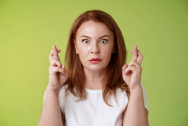 Stunned intense worried middle-aged redhead woman stare nervously awaiting important result implore dream come true receive positive reply standing stupor green background make wish good luck - Photo, Image
