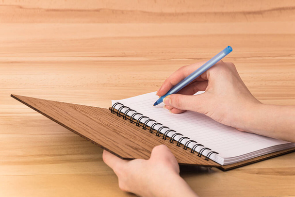 Egy férfi tollal ír egy nyitott jegyzetfüzetben, fehér oldalakkal és egy fa barna doboz rugós borítással, ami az asztalon fekszik. - Fotó, kép