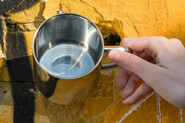Kubek ze stali nierdzewnej do napojów jest trzymany w dłoni na tle malowanej ściany betonowej - Zdjęcie, obraz