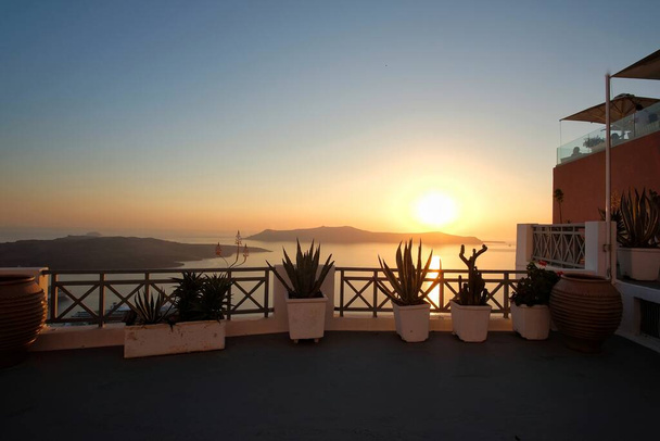 Panoramic view of the volcano Nea Kameni  from a rooftop decorated with flower pots in Santorini at sunset - Foto, Bild