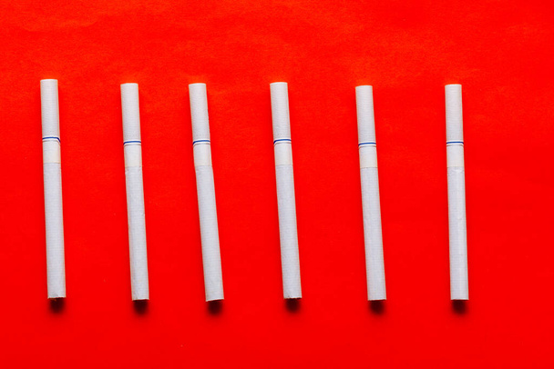 Cigarrillos blancos al fondo rojo. Nicotina en el tabaco  - Foto, imagen