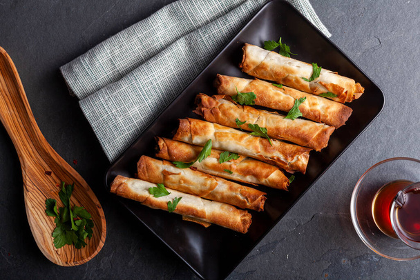 Traditional Turkish sigara boregi, a phyllo dough roll with cheese or ground meat stuffing. Deep fried rolls are served on a tray with parsley leaves as topping and Turkish tea on the side. - 写真・画像