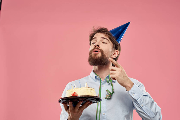 Man with cake in a plate and in a blue shirt on a pink background birthday holidays cropped view - Foto, afbeelding