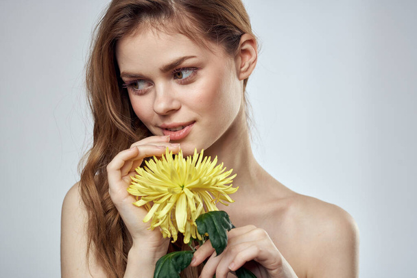 Portret van een mooie vrouw met een gele bloem op een lichte achtergrond bijgesneden met Copy Space Model - Foto, afbeelding