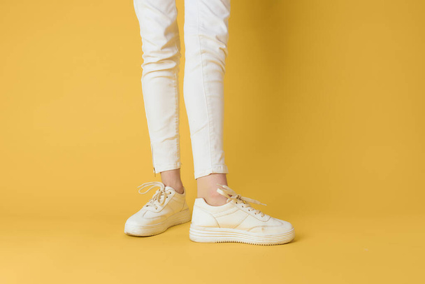 Female feet white sneakers attractive look fashion yellow background - Photo, Image