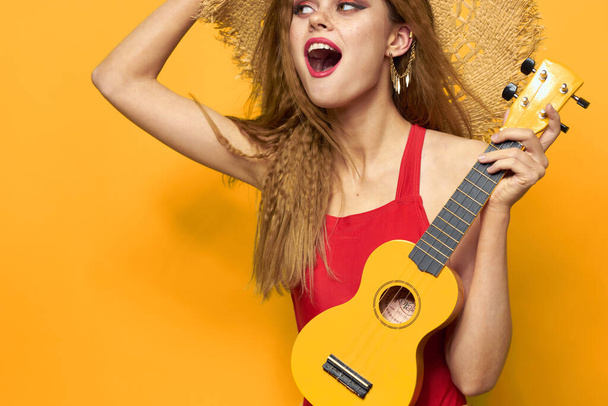 femme en chapeau rouge ukulele dans les mains style de vie été t-shirt rouge fond jaune - Photo, image