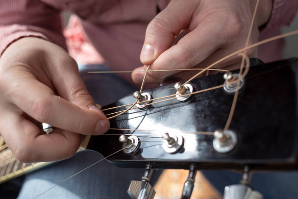 Руки чоловіка вставляють нові струни в акустичну гітару. Ремонт музичних інструментів
.  - Фото, зображення