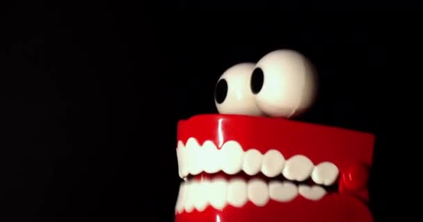 Een speelgoedprothese met witte tanden en grote ogen, op een zwarte achtergrond. - Video